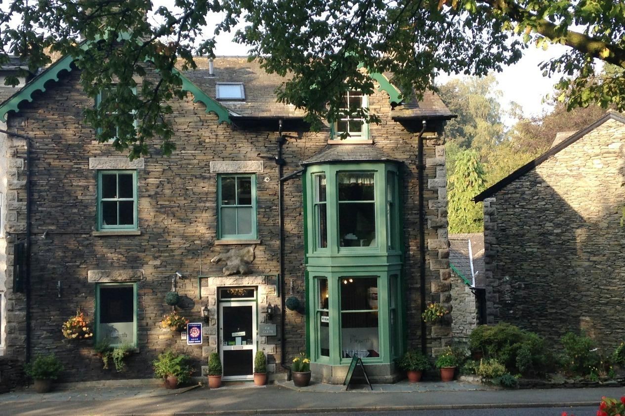 The Firgarth, a Lakeland stone house with green bay window frames, by day
